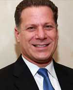 The image features a man with a smile, wearing a dark suit and tie, against a light background.