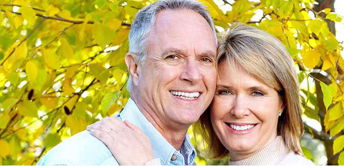 An elderly couple posing together for a photo with autumn leaves in the background.