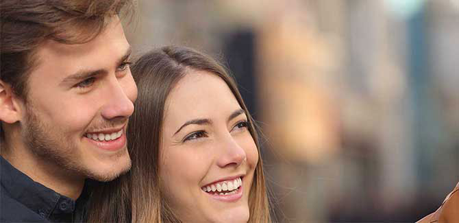 A young couple smiling at each other against a blurred cityscape background.