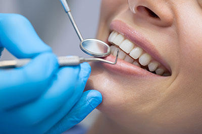 The image depicts a person receiving dental care, with a dentist using a dental drill on their teeth while wearing protective gloves and a face mask.
