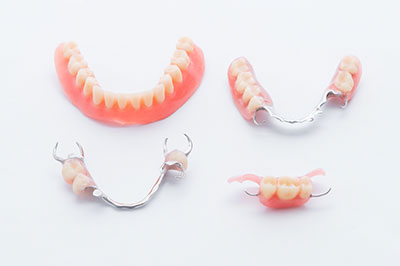 The image shows four dental bridges with artificial teeth displayed on a white background. Each bridge has a different design and color scheme, showcasing various options for dental restoration.
