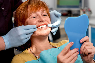 A woman receiving dental care with a smiling expression, holding up an impression mold while wearing a blue surgical mask.