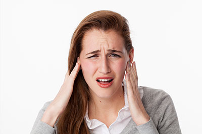The image shows a woman with her hand on her head, possibly indicating pain or discomfort, set against a white background.