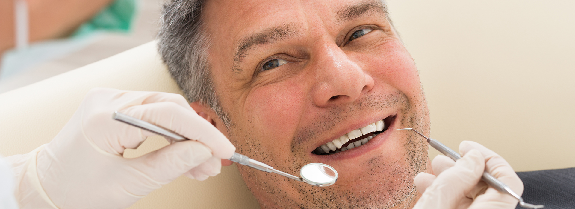 A man sitting in a dentist s chair with a dental professional working on his teeth, wearing a surgical mask and gloves.