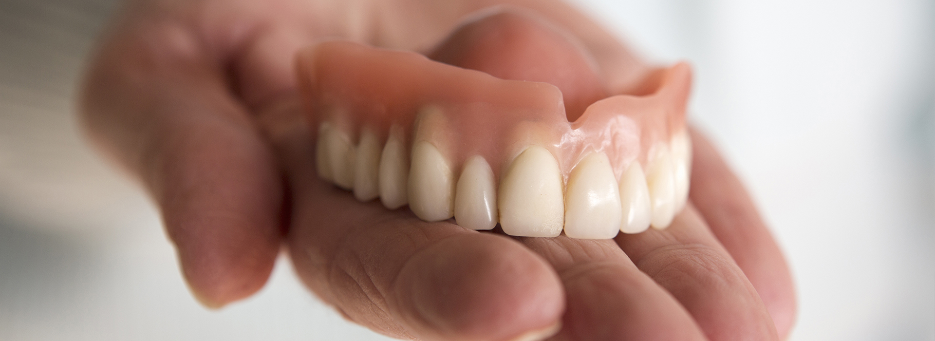 An individual s hand holding a set of artificial teeth with a clear background.