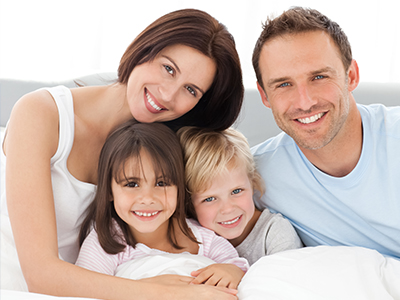 A family of four, including two adults and two children, posing for a photo on a bed with a happy expression.